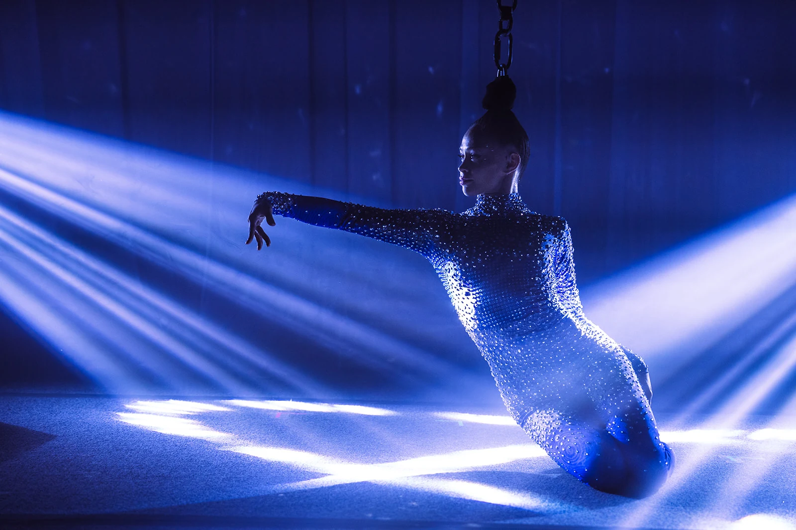 Tink in profile during a Cirque Frost performance, wearing a crystal-encrusted catsuit lit in blue stage light