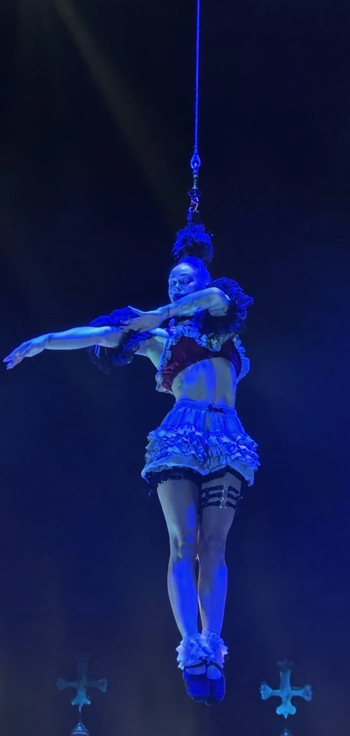 Tink hanging by her hair with arms swept wide, washed in deep blue light