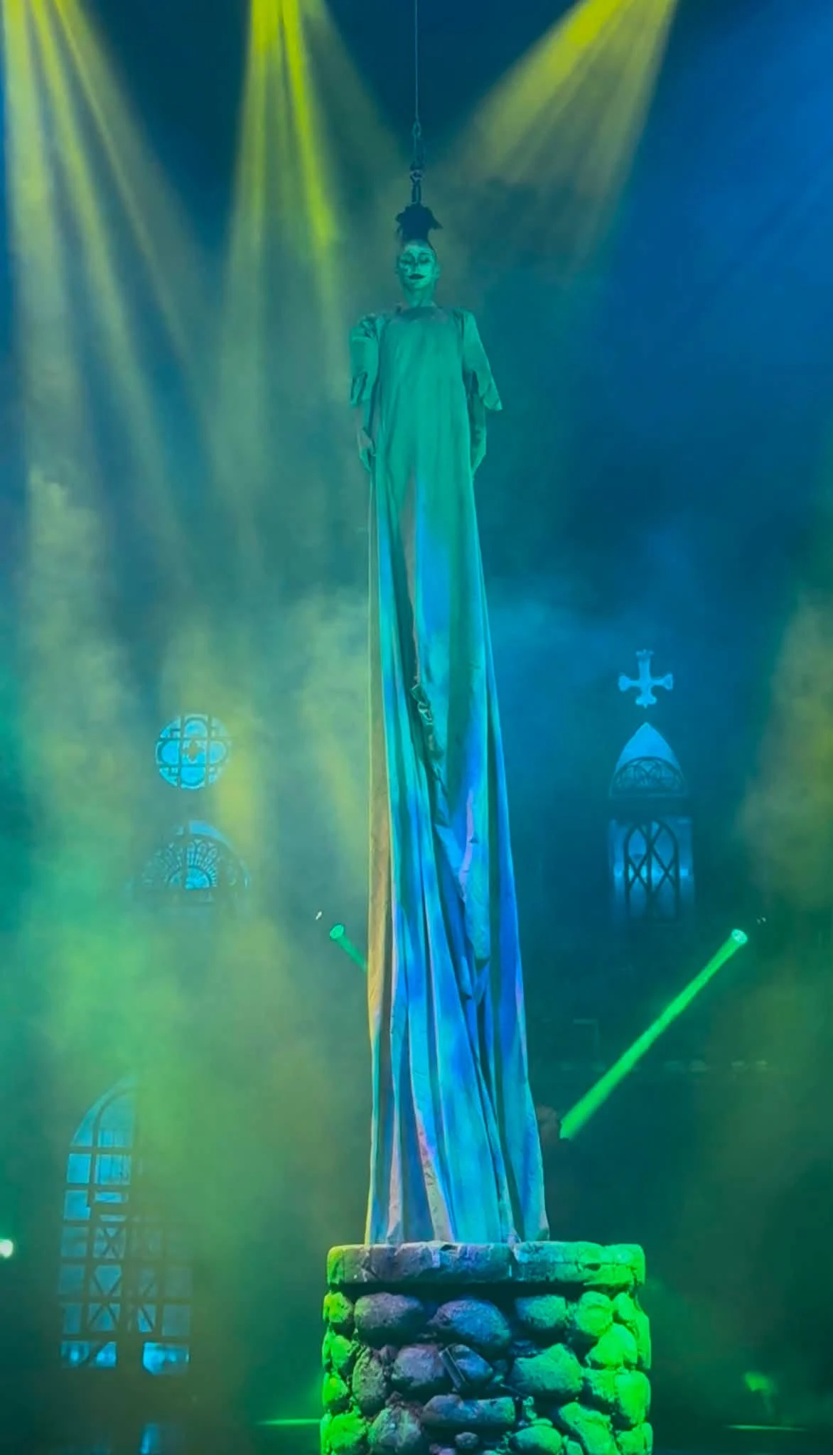 Tink as a towering robed figure in green stage haze during the show's character work